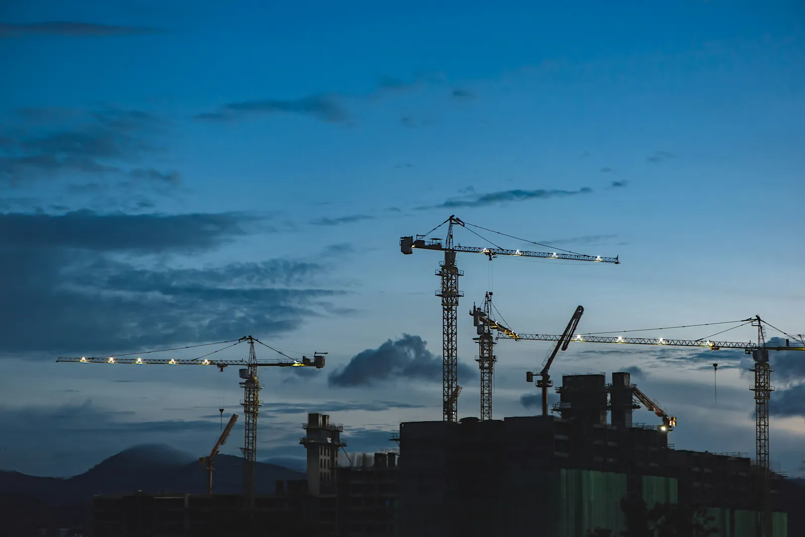 Tower cranes above a construction site at dusk.